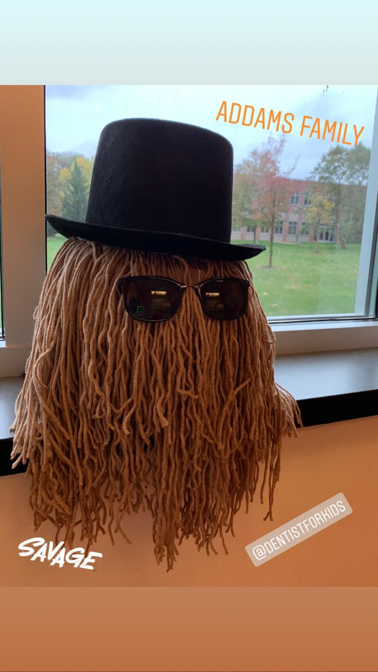 an odd looking stuffed animal with sunglasses and a hat on it's head, sitting in front of a window