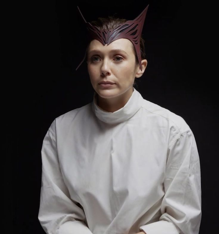 a woman wearing a white shirt with horns on her head and hands folded in front of her chest