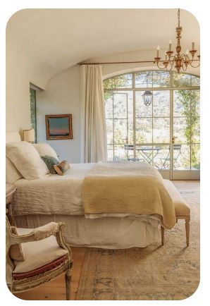 a bedroom with a bed, chair and chandelier in front of a large window