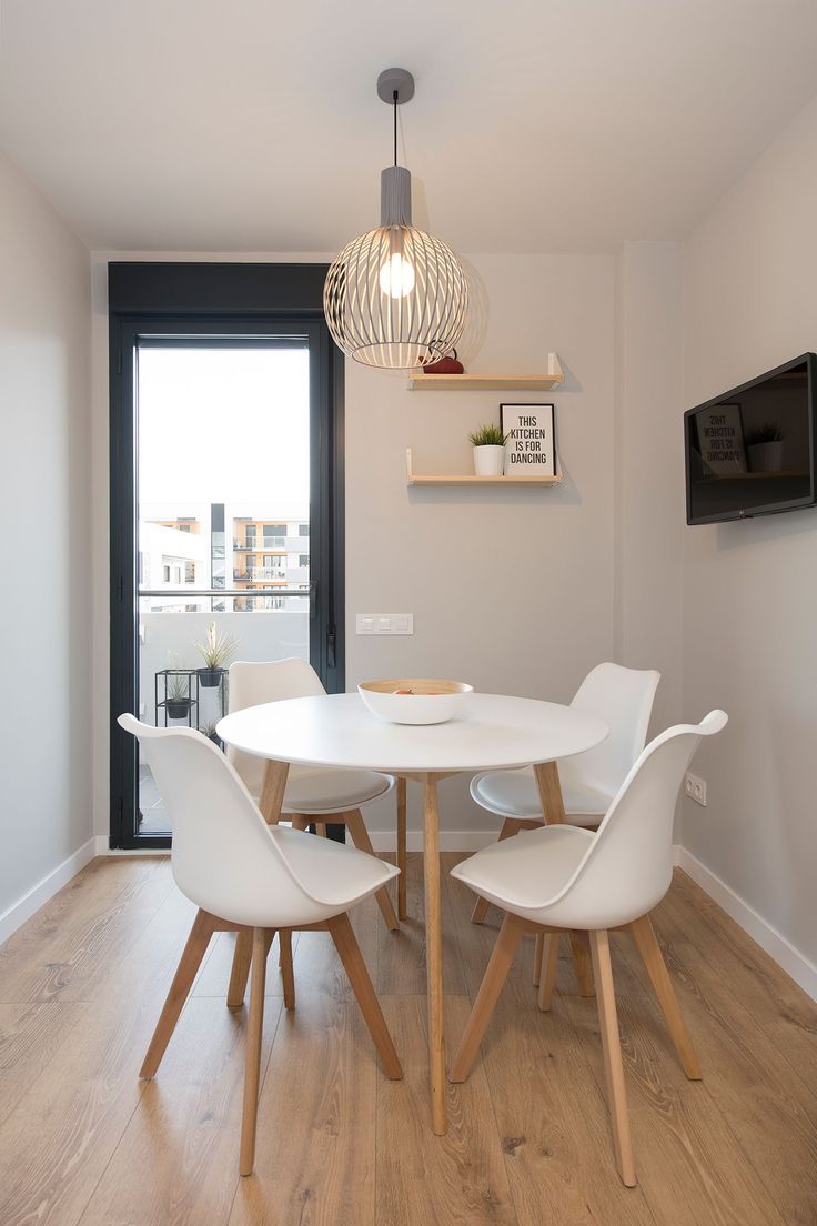 a dining room table with white chairs and a television mounted on the wall behind it