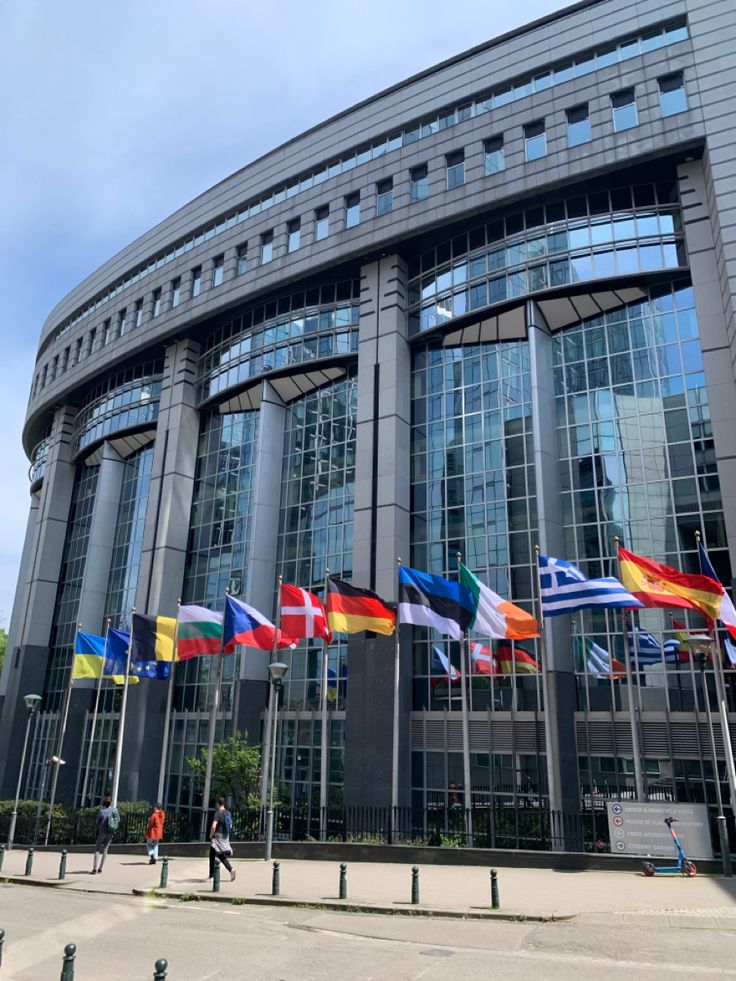 several flags are flying in front of a large building with many windows on the sides