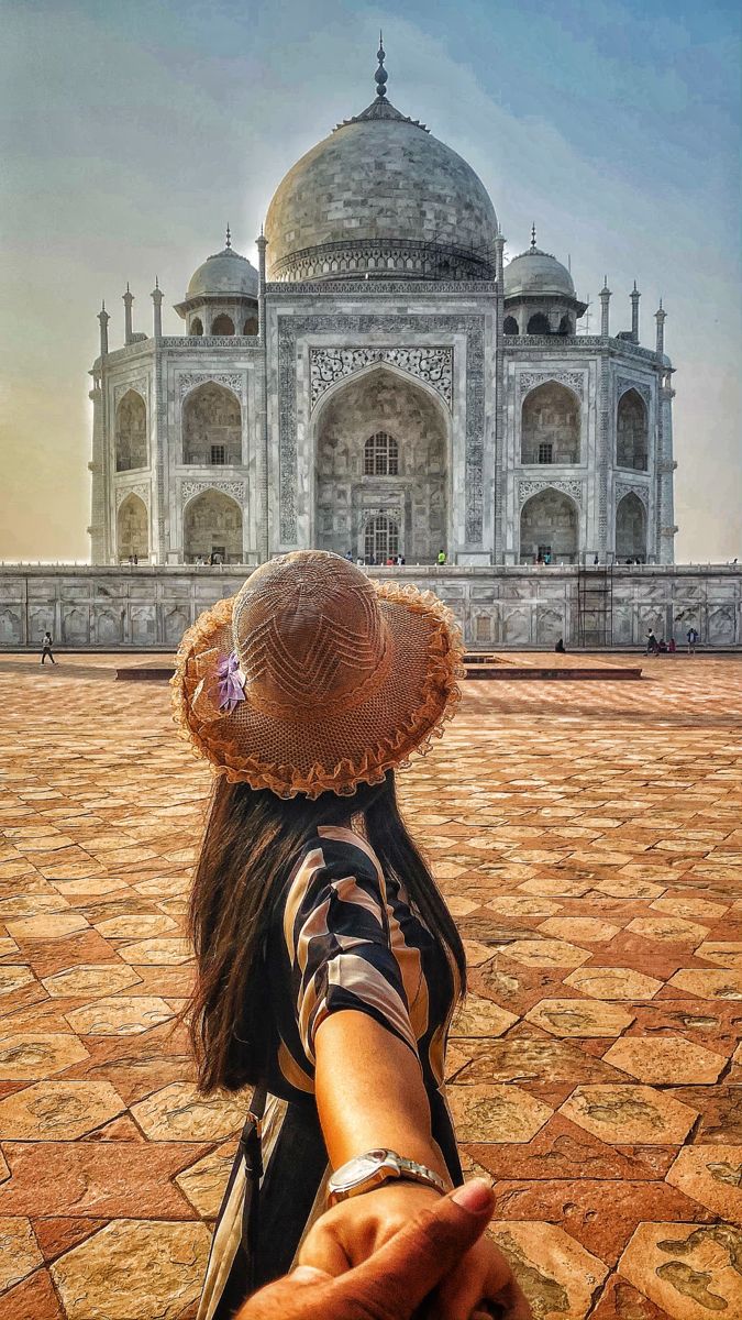 a woman with a straw hat standing in front of the tajwa mosque, india