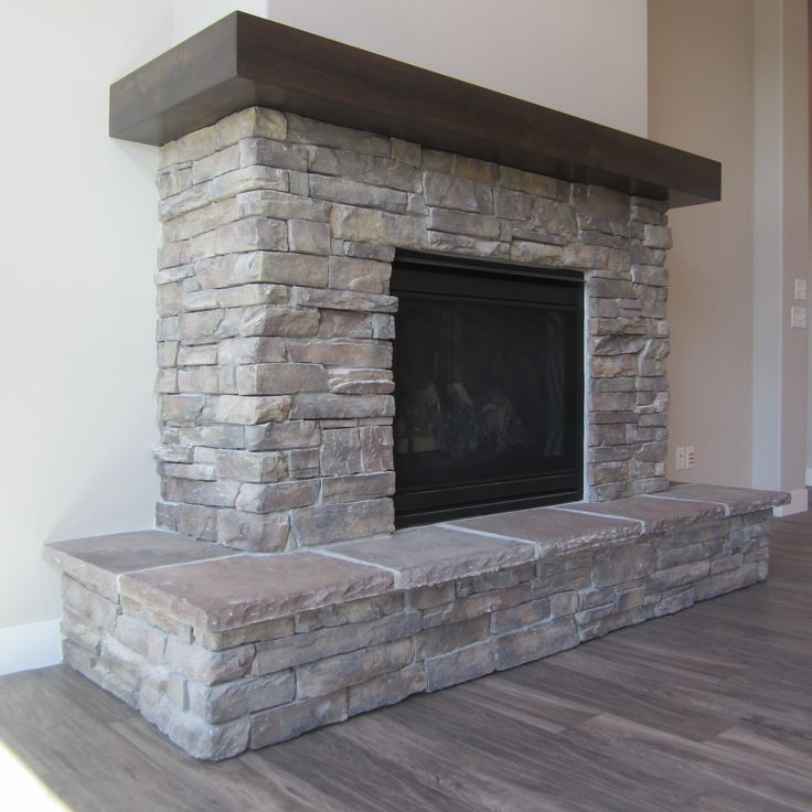 a stone fireplace in the corner of a room with wood flooring and white walls