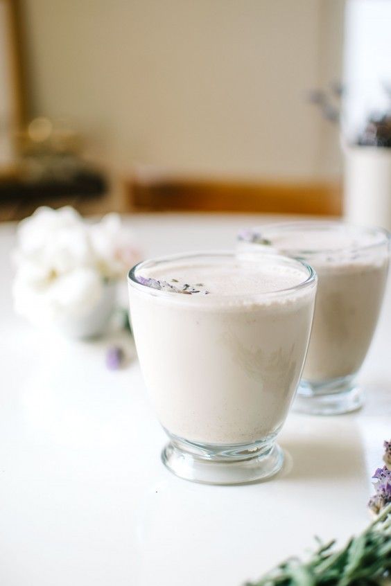 two glasses filled with white liquid sitting on top of a table next to lavender flowers