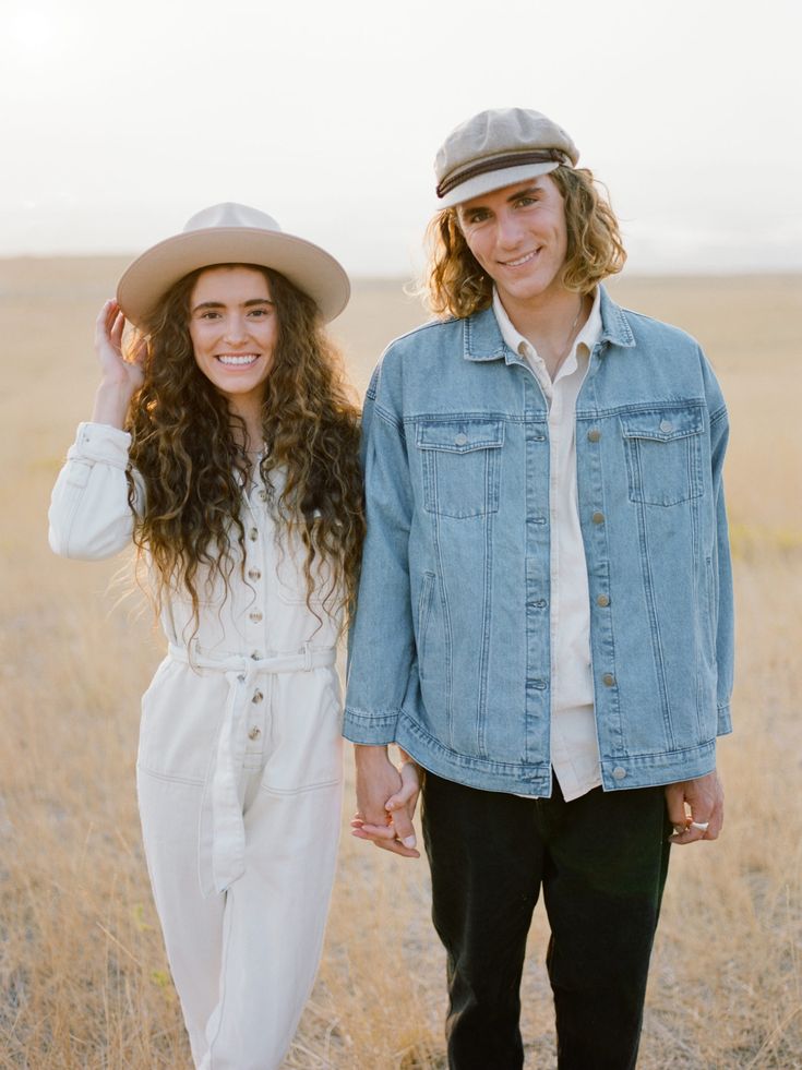 a man and woman holding hands while standing in the middle of a field with tall grass