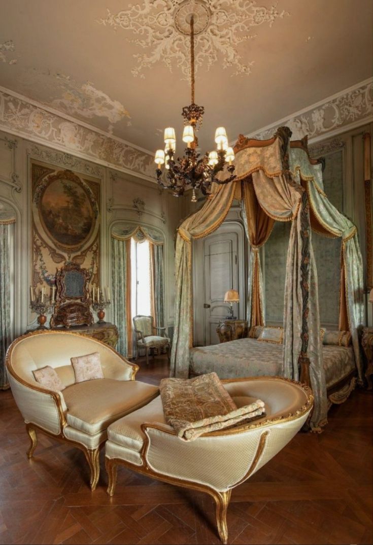 an ornate bedroom with four poster bed, chandelier and two chairs in it