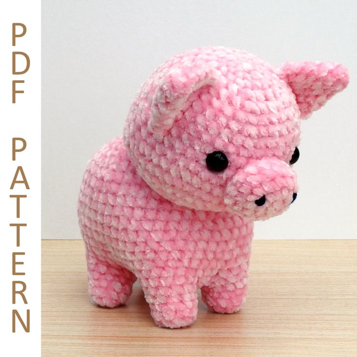 a pink crocheted pig sitting on top of a wooden table next to a white wall