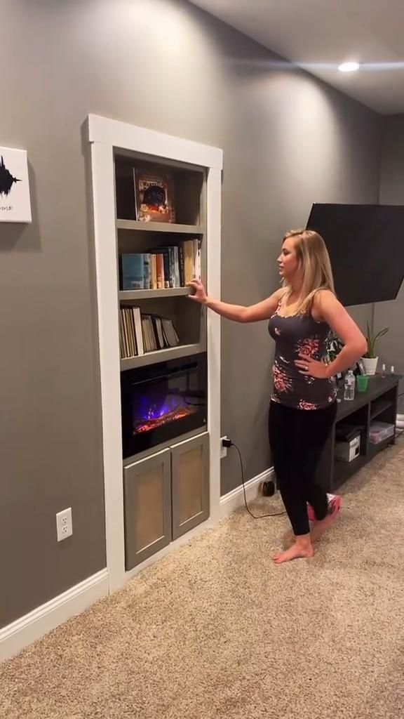 a woman is standing in front of a book shelf and pointing at something on the wall