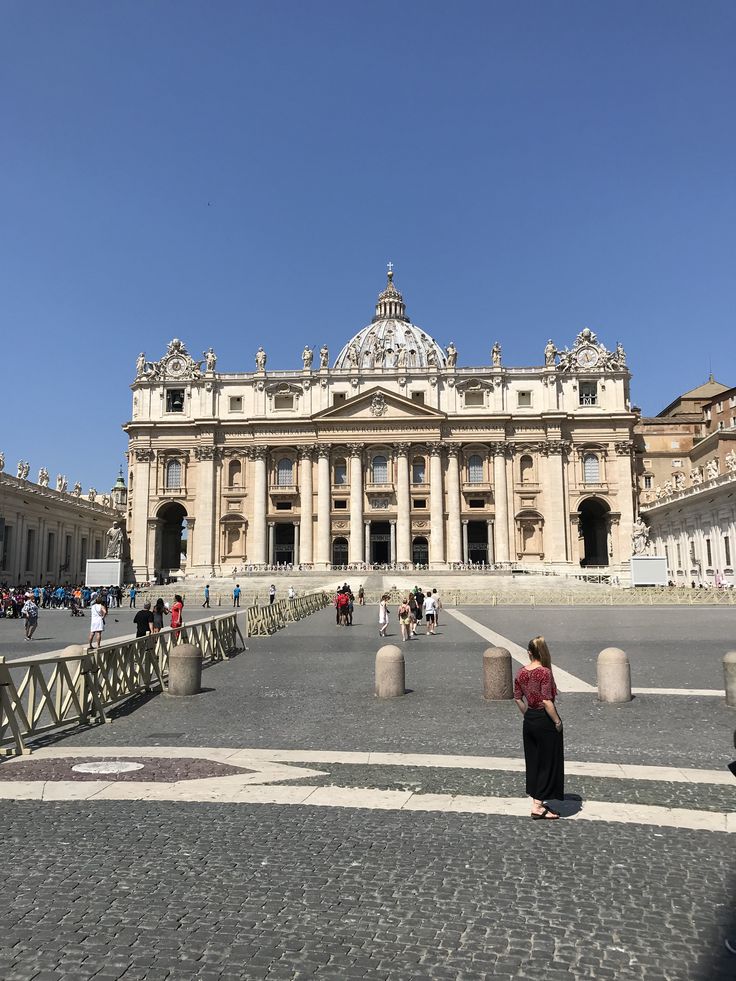 a woman standing in front of a large building with lots of people walking around it