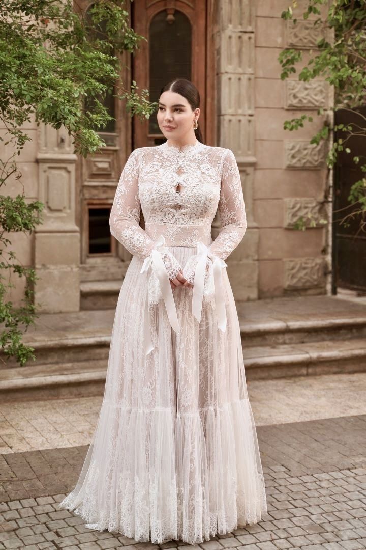 a woman in a long white dress standing on a brick walkway with trees behind her