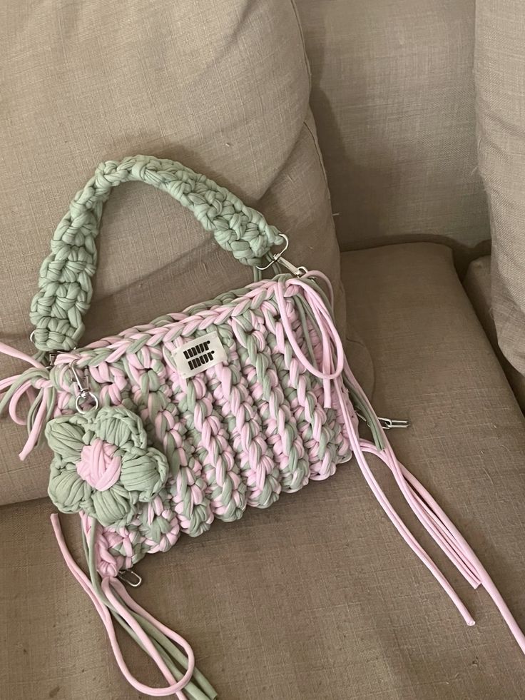 a pink and green handbag sitting on top of a couch next to a pillow