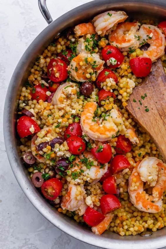 a pot filled with shrimp, corn and tomatoes on top of a table next to a wooden spoon