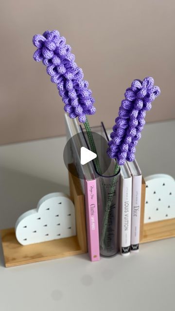 two purple flowers are in a glass vase with books on the shelf next to it