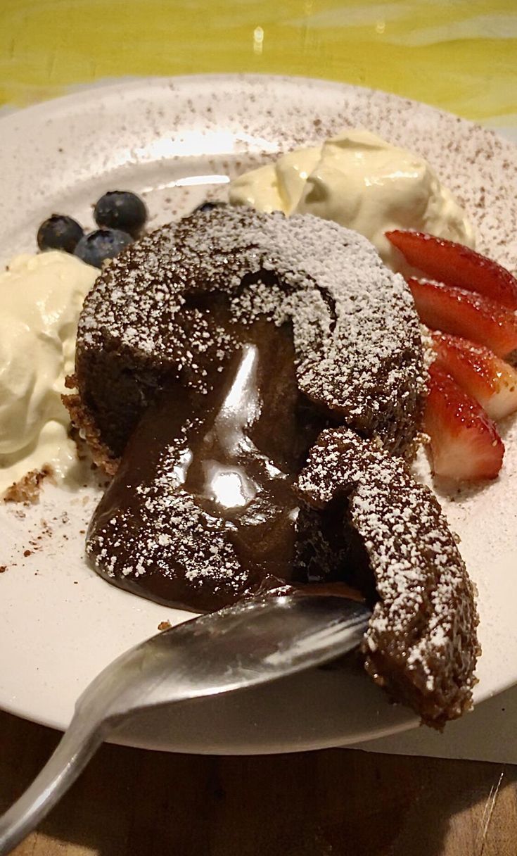 a white plate topped with chocolate cake covered in powdered sugar and strawberries next to whipped cream