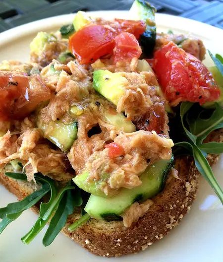 an open face sandwich with tomatoes, cucumbers and other toppings on a white plate