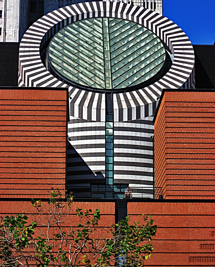 a large clock on the side of a building with a tree in front of it