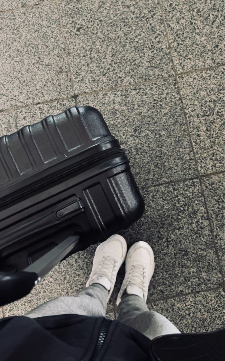 a person standing next to a black piece of luggage on top of a cement floor