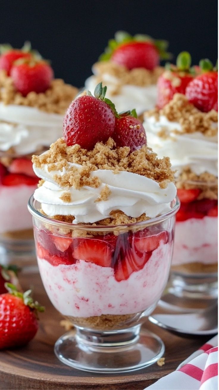 three desserts with strawberries and whipped cream in glass dishes on a wooden table