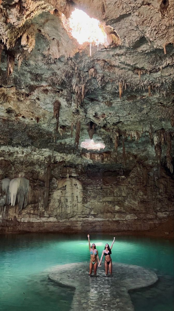 two women standing in the water at an underground cave with blue and green colored water