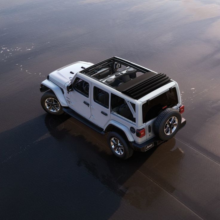 a white jeep is parked on the wet sand by the water's edge,