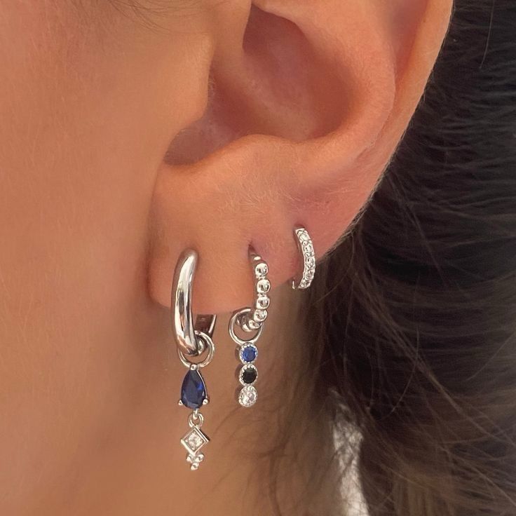 a woman's ear is shown with three different colored stones and two silver hoop earrings