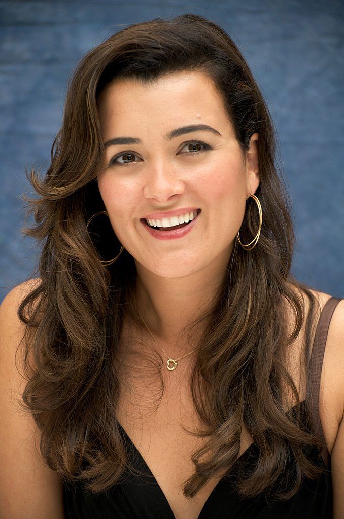 a woman with long brown hair and large hoop earrings smiles at the camera while wearing a black dress