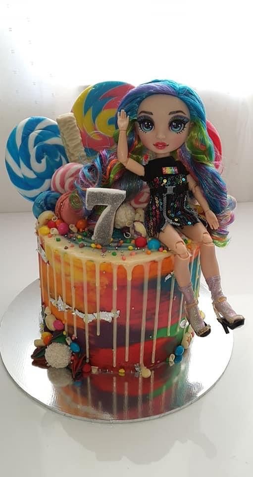 a birthday cake with a doll on top and lollipops in the background