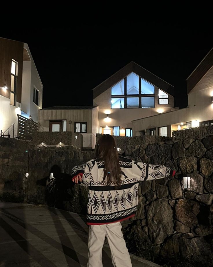 a person standing on a sidewalk in front of a house at night with their arms outstretched