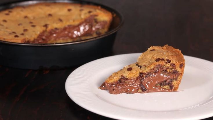 a piece of chocolate chip pie on a white plate next to a pan of cake