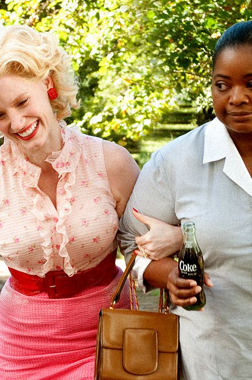 two women standing next to each other holding bottles and purses, one woman is smiling at the camera