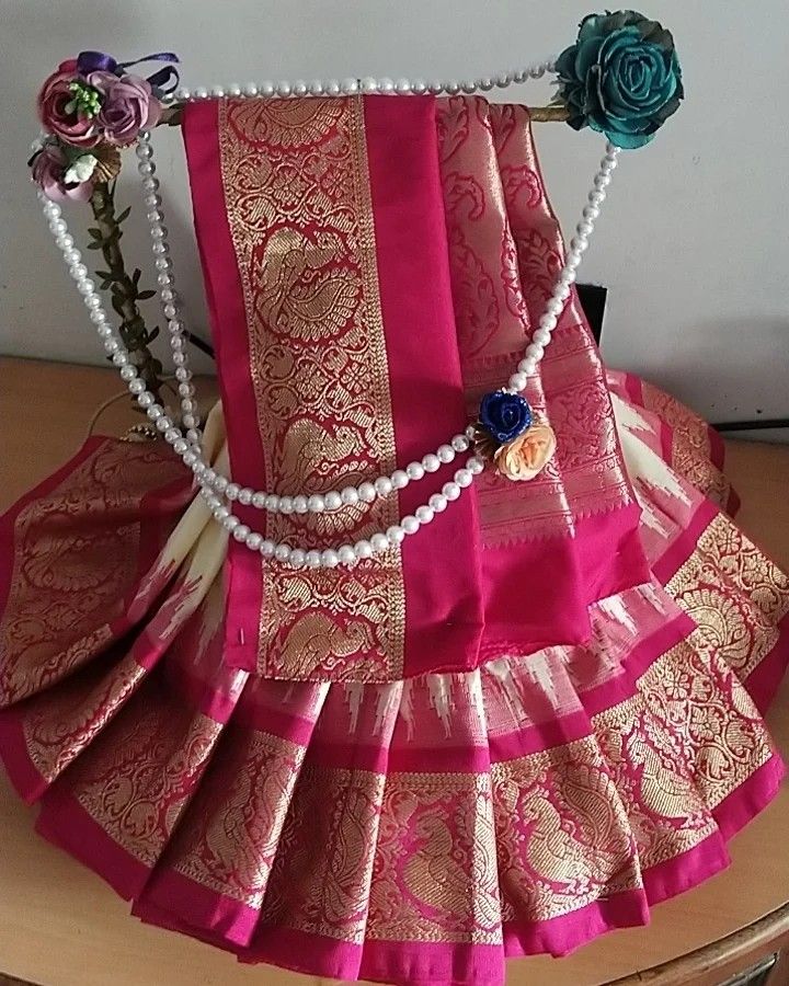 a pink and gold saree with pearls on the neck is sitting on a table