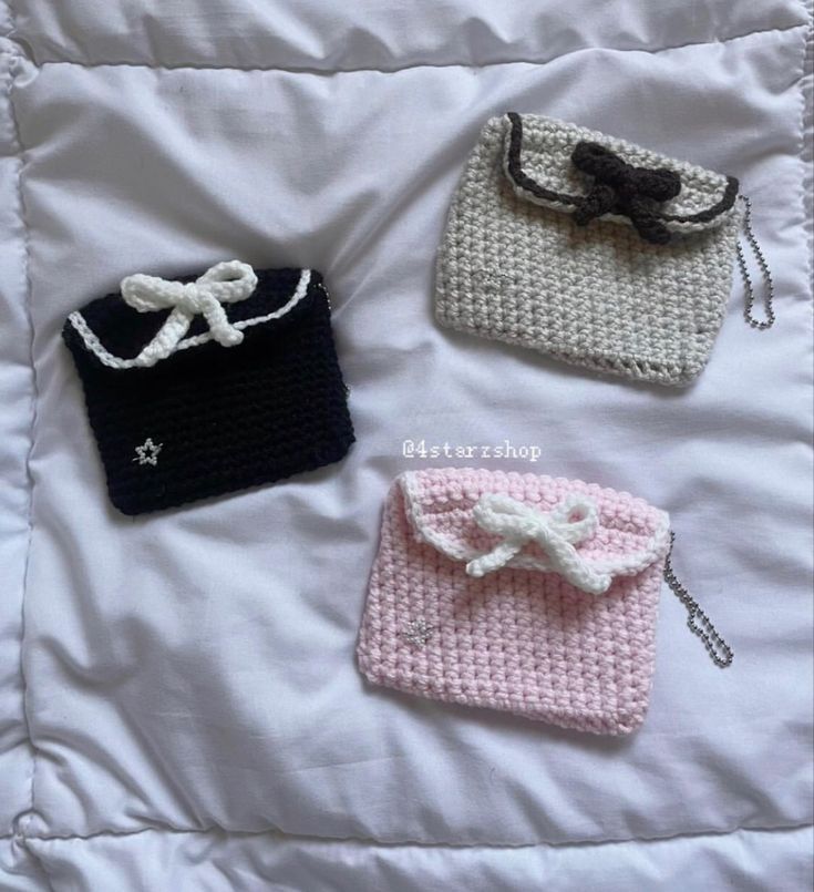 three crocheted purses are laying on a bed together, one has a bow