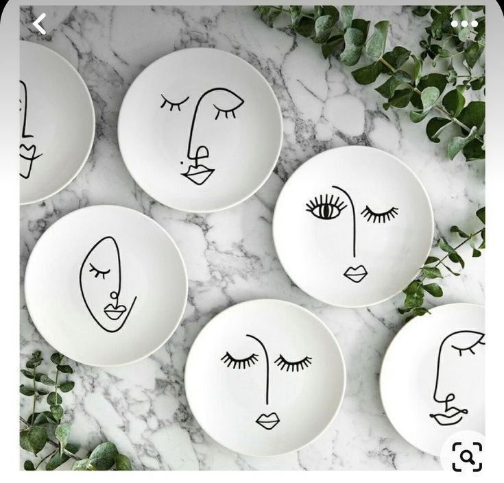 four plates with faces drawn on them sitting on a marble counter top next to green leaves