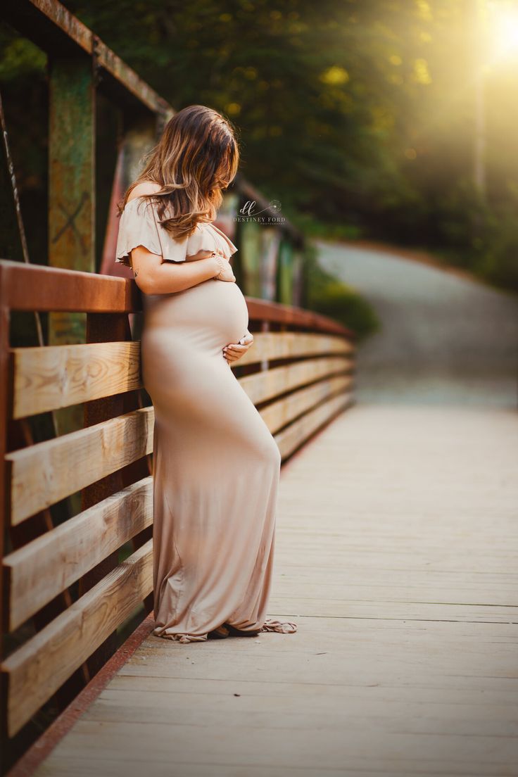 a pregnant woman leaning against a wooden fence