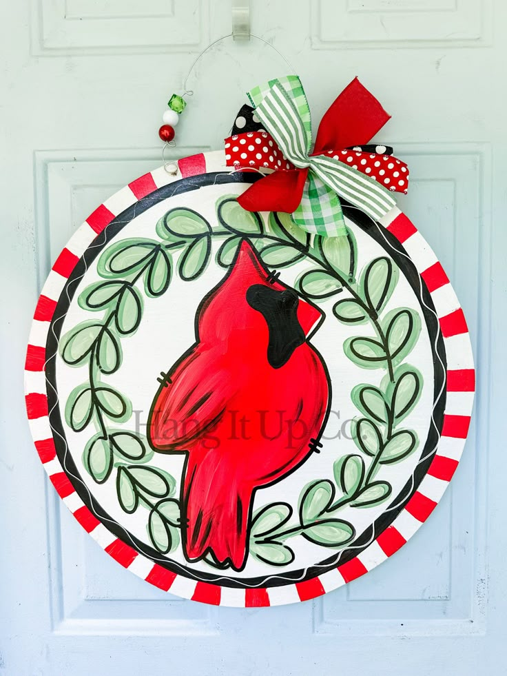 a red and white wreath with a cardinal painted on it is hanging on the front door