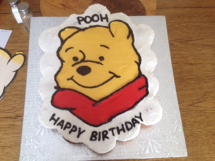 a winnie the pooh birthday cake is sitting on a table next to a cookie