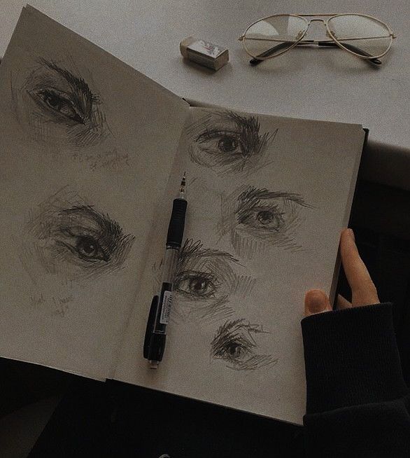 a person holding an open book with eye drawings on it next to a pair of glasses