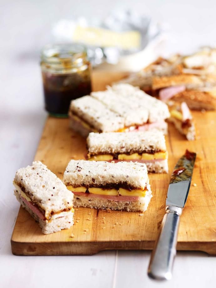 a cutting board with sandwiches on it next to a knife and jar of jams