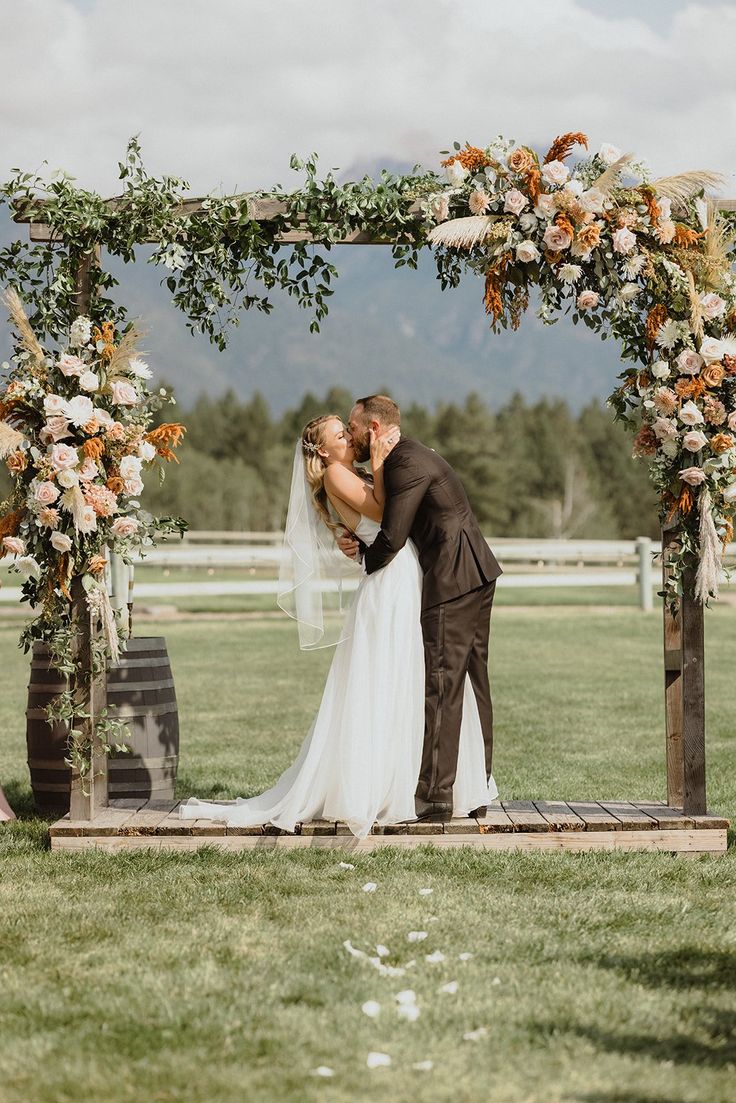 a bride and groom kissing under an arch decorated with flowers