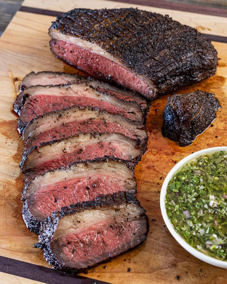 sliced steak on a cutting board next to a small bowl of salsa