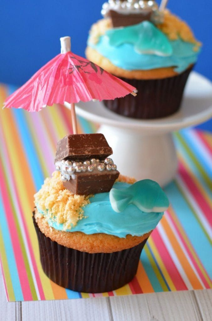 two cupcakes with blue frosting and chocolate on top, one has an umbrella