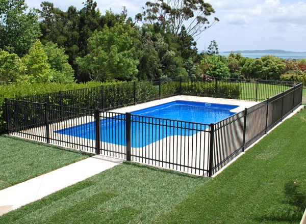 an above ground pool surrounded by black fence and green grass with trees in the background