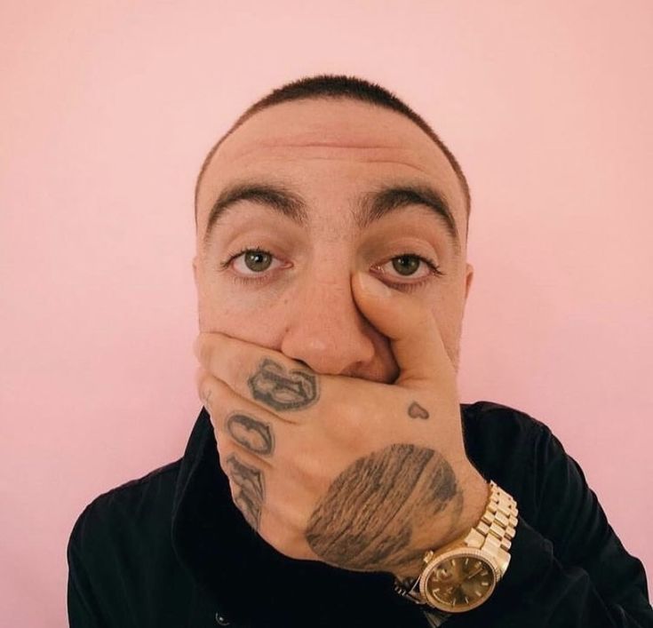 a man covering his mouth with both hands and looking at the camera while standing against a pink wall