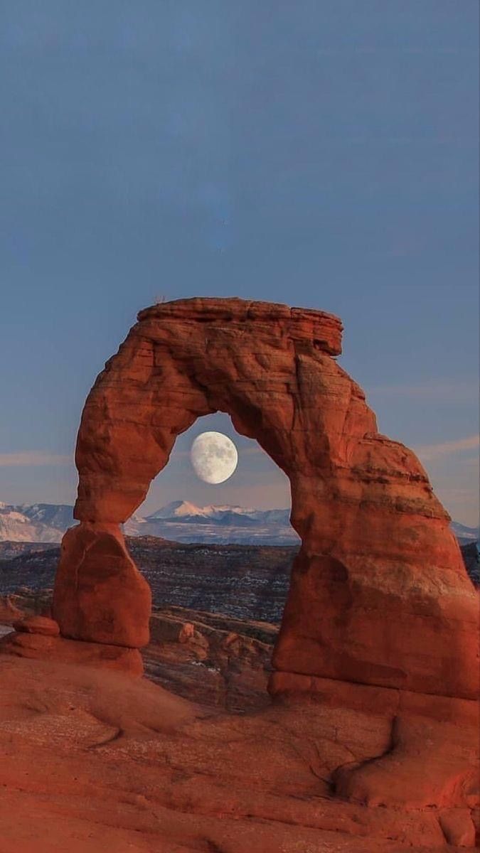 the moon is setting over arches and mountains