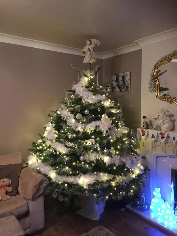 a white christmas tree in a living room with blue lights on the floor and a fireplace