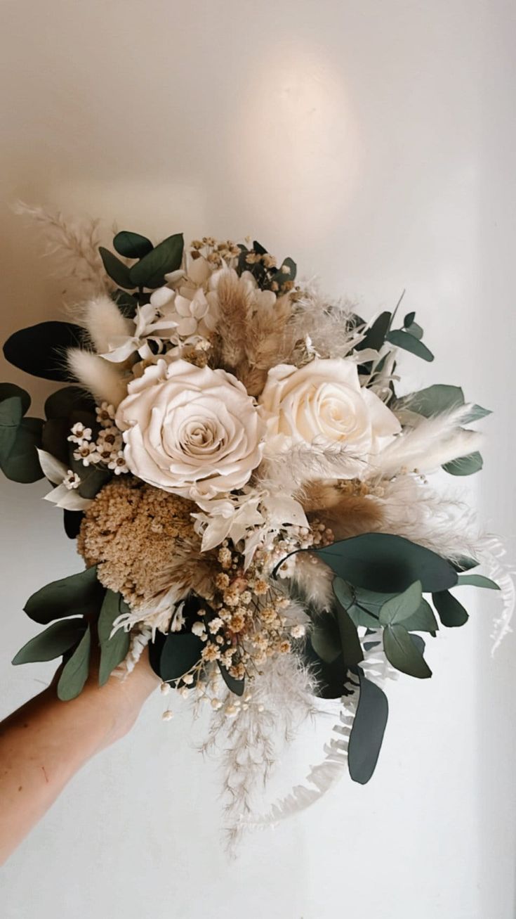 a person holding a bouquet of flowers in their hand with greenery on the side