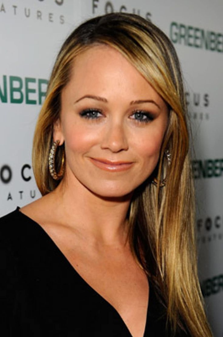 a woman with long blonde hair smiling at the camera and wearing large gold hoop earrings