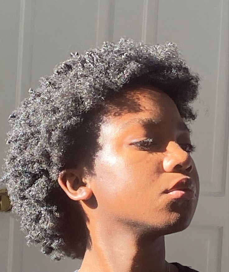 a young man with an afro looks off into the distance while standing in front of a garage door