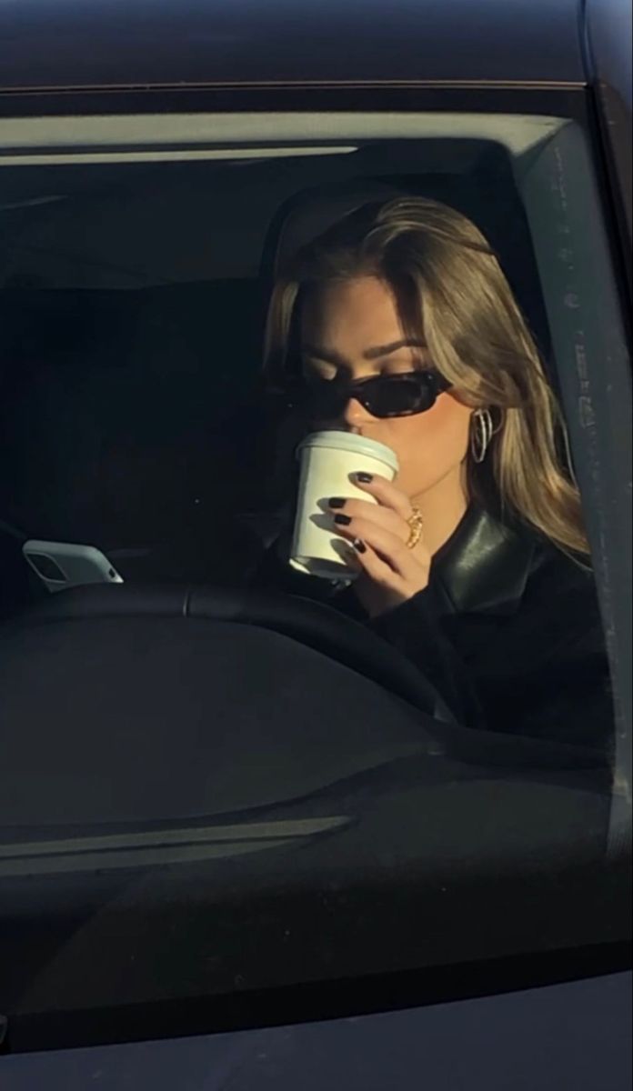 a woman sitting in the back seat of a car drinking from a coffee cup