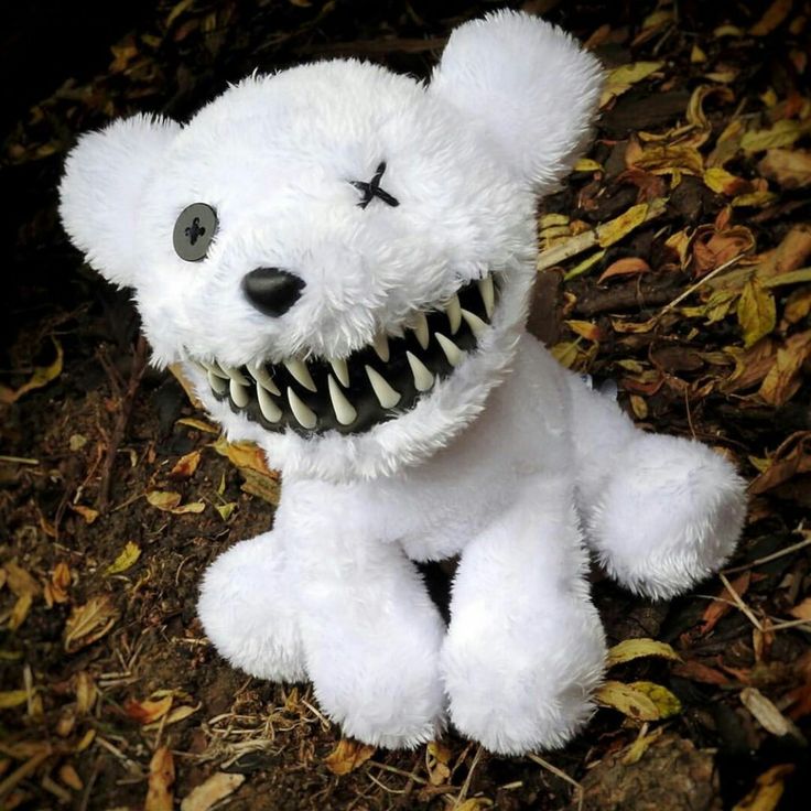 a white teddy bear with teeth and fangs on it's face sitting in the leaves